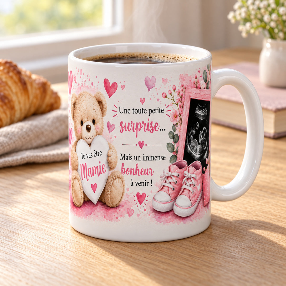 Mug Tu vas être Mamie « Annonce Grossesse » posé sur une table en bois avec un croissant, pause café