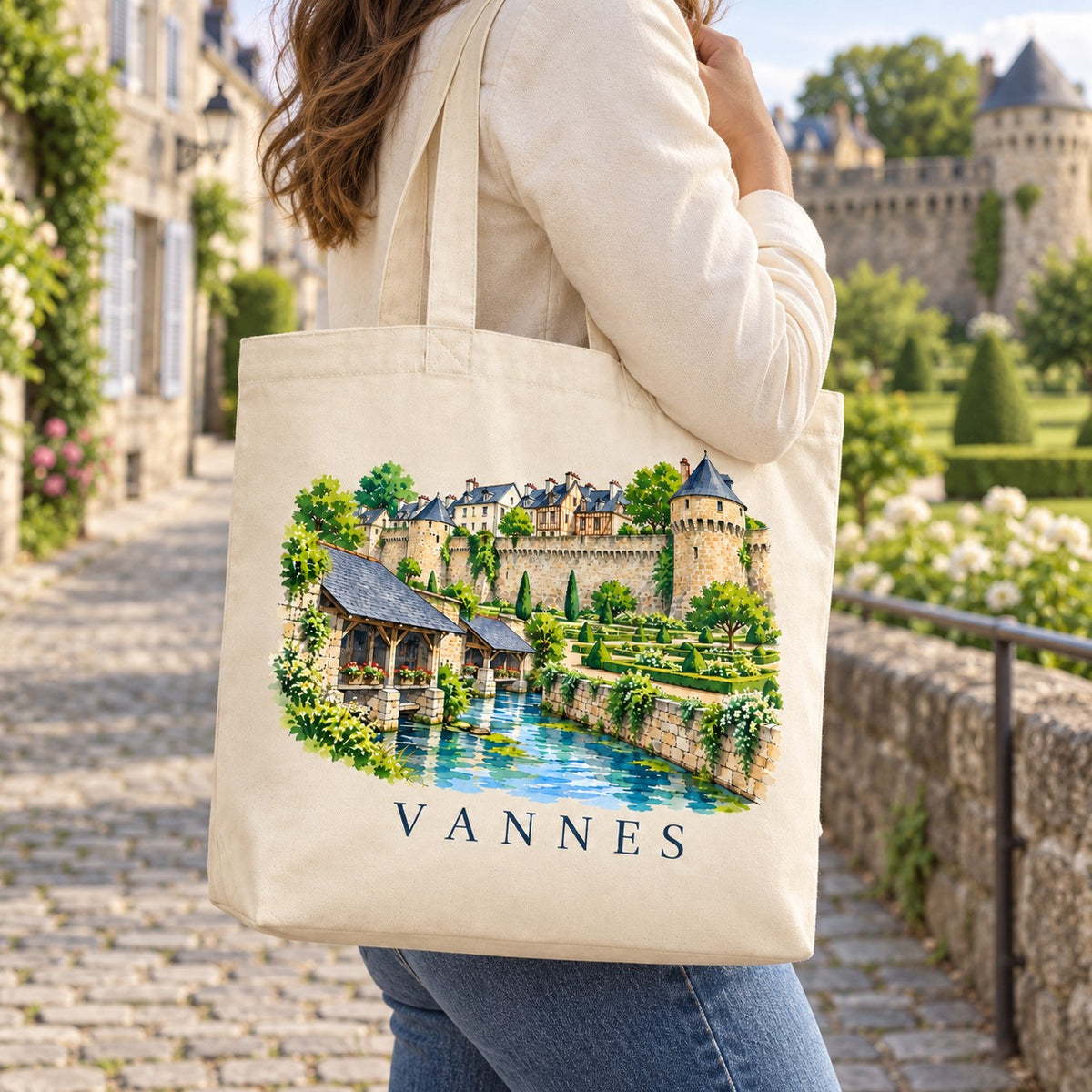 Tote bag Vannes Premium porté à l'épaule dans une rue pavée de la vieille ville, remparts en arrière-plan