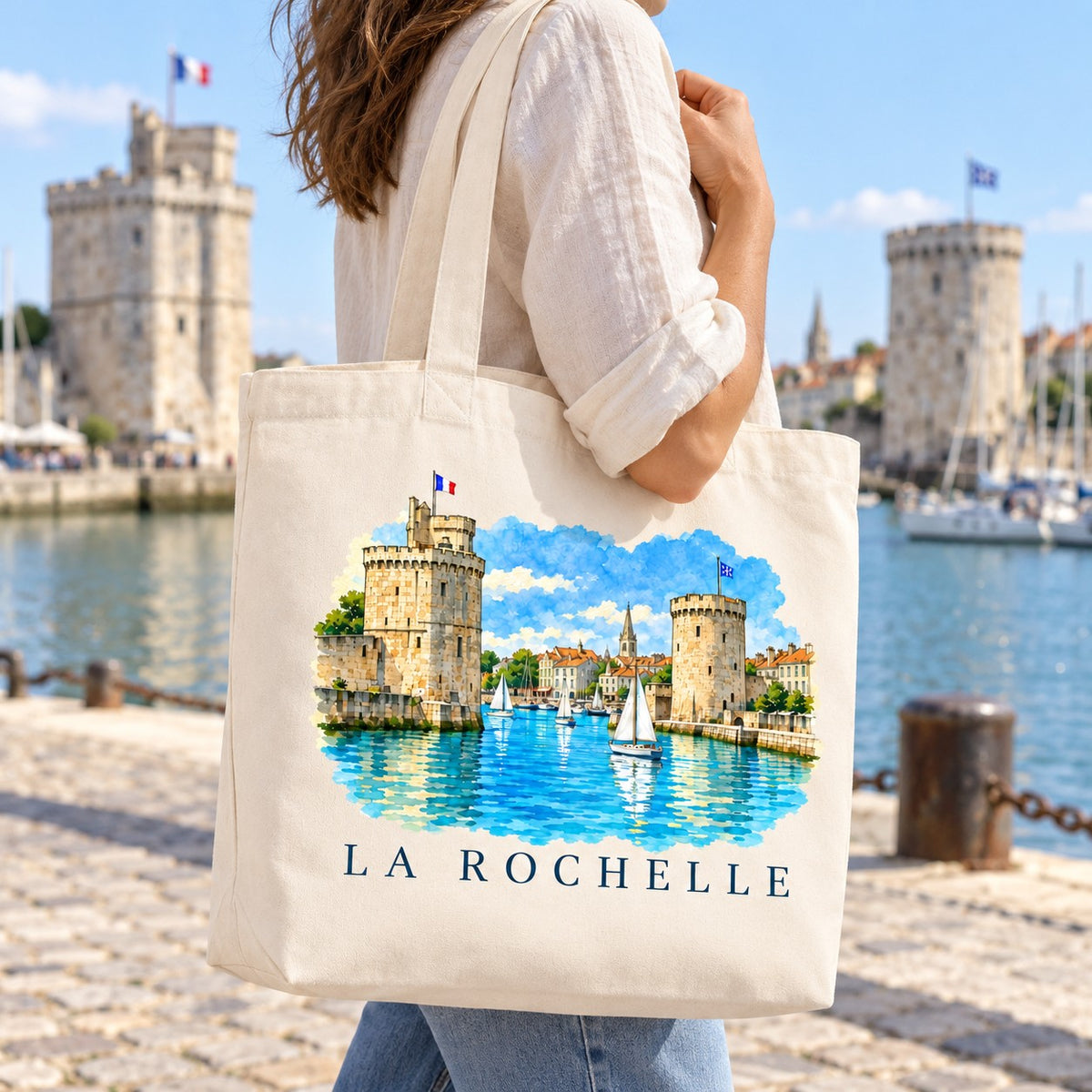 Tote bag La Rochelle Premium porté à l'épaule sur le quai du Vieux-Port, tours en arrière-plan
