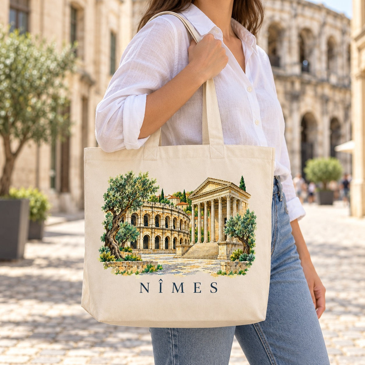 Tote bag Nîmes Premium porté à l'épaule dans une rue pavée, arènes en arrière-plan