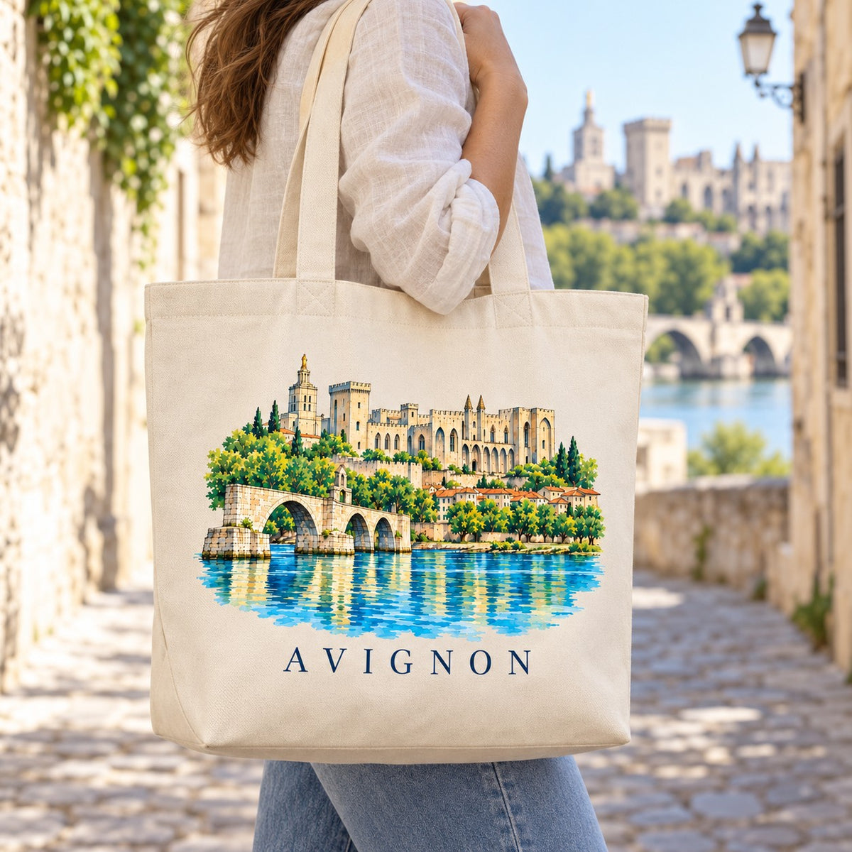 Tote bag Avignon Premium porté à l'épaule dans une ruelle, palais des Papes et Rhône en arrière-plan