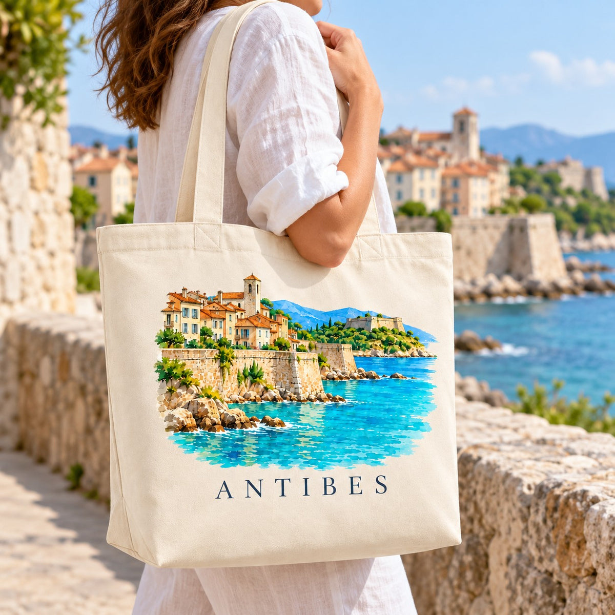 Tote bag Antibes Premium porté à l'épaule sur les remparts, vieille ville et mer en arrière-plan