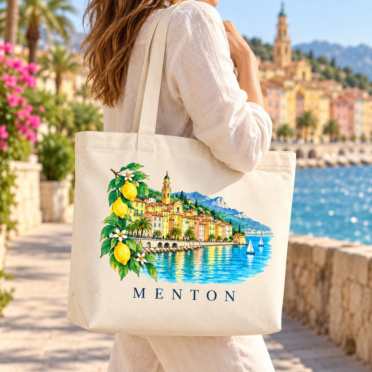 Tote bag Menton Premium porté à l'épaule sur la promenade, vieille ville en arrière-plan