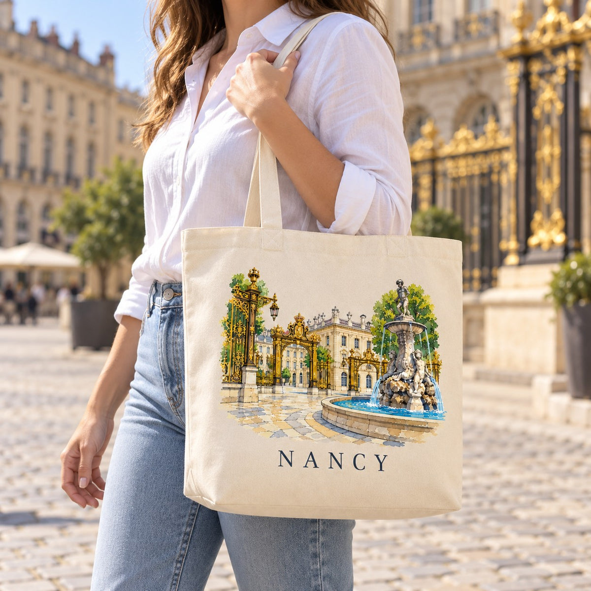 Tote bag Nancy Premium porté à l'épaule sur la place Stanislas, grilles dorées en arrière-plan