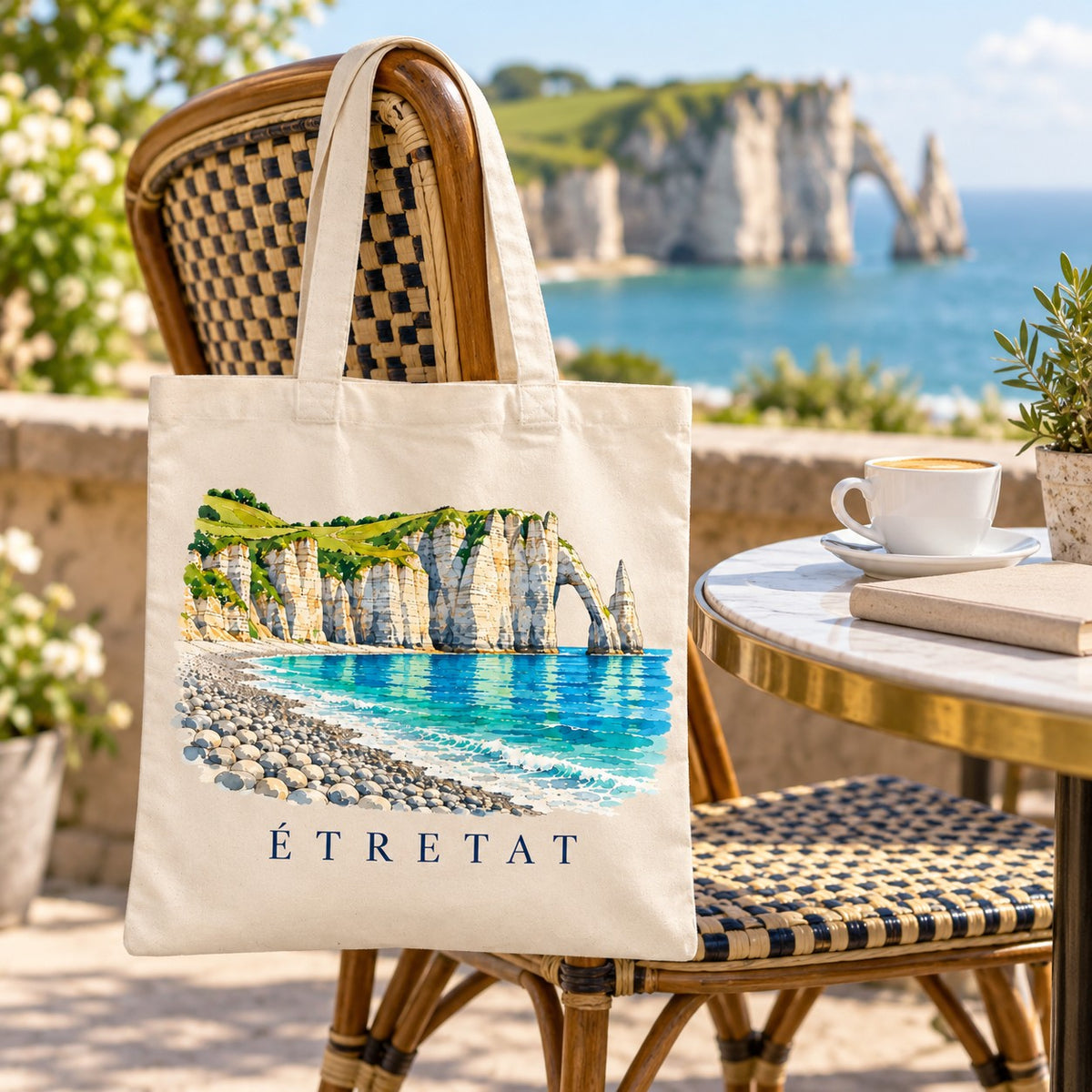 Tote bag Étretat Essentiel suspendu à une chaise en terrasse face aux falaises, avec un café
