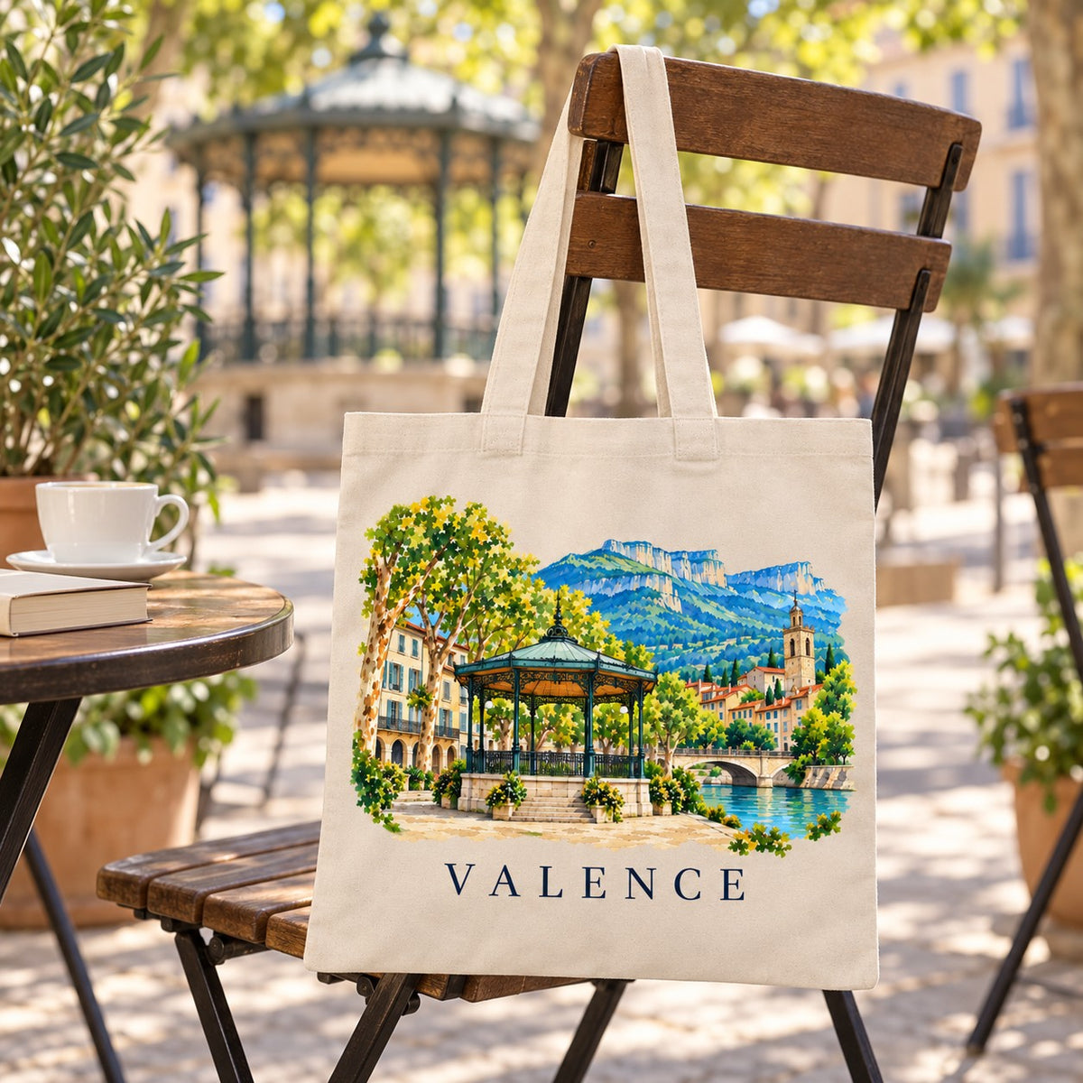 Tote bag Valence Essentiel suspendu à une chaise en terrasse face au kiosque à musique, avec un café