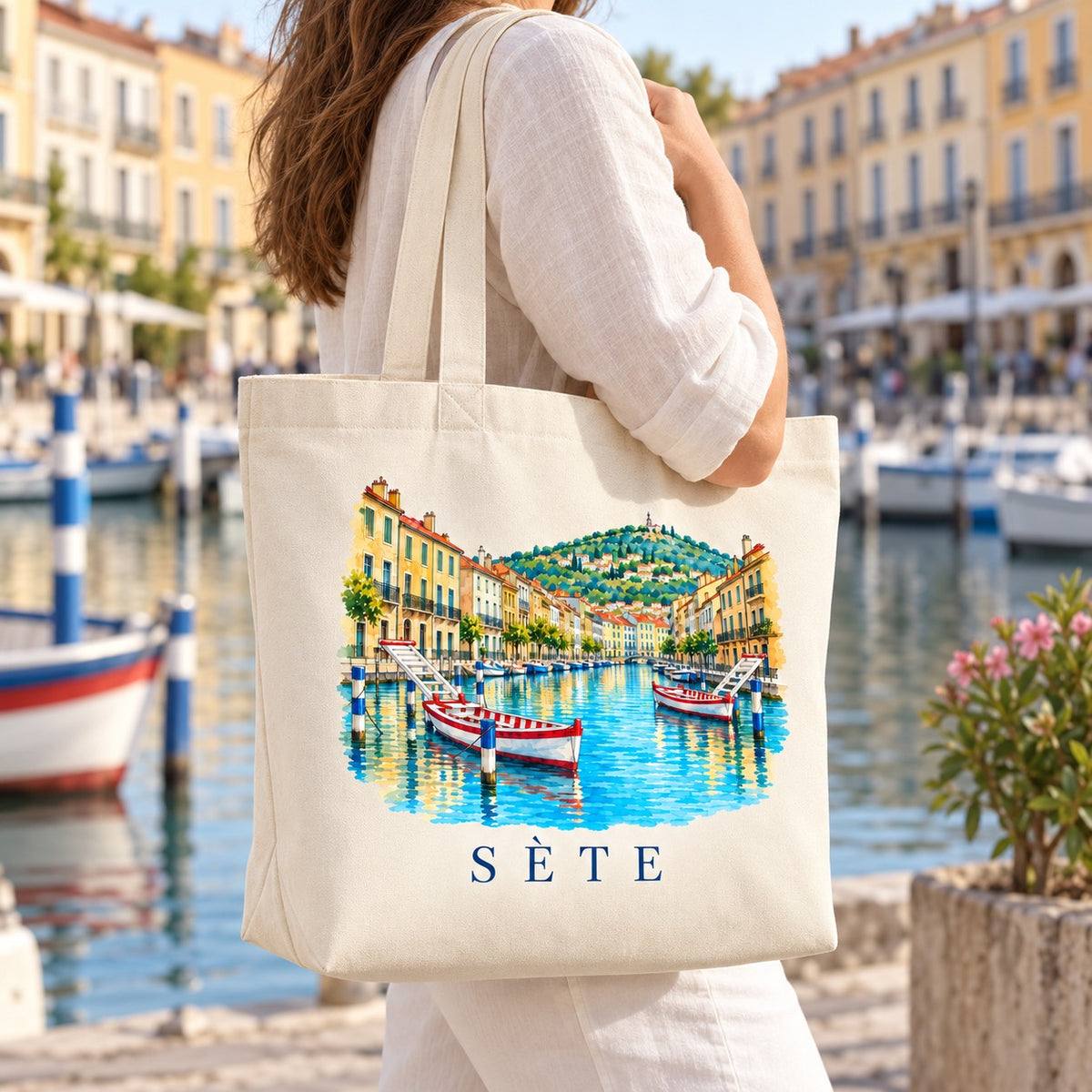 Tote bag Sète Premium porté à l'épaule sur un quai du canal, barques en arrière-plan