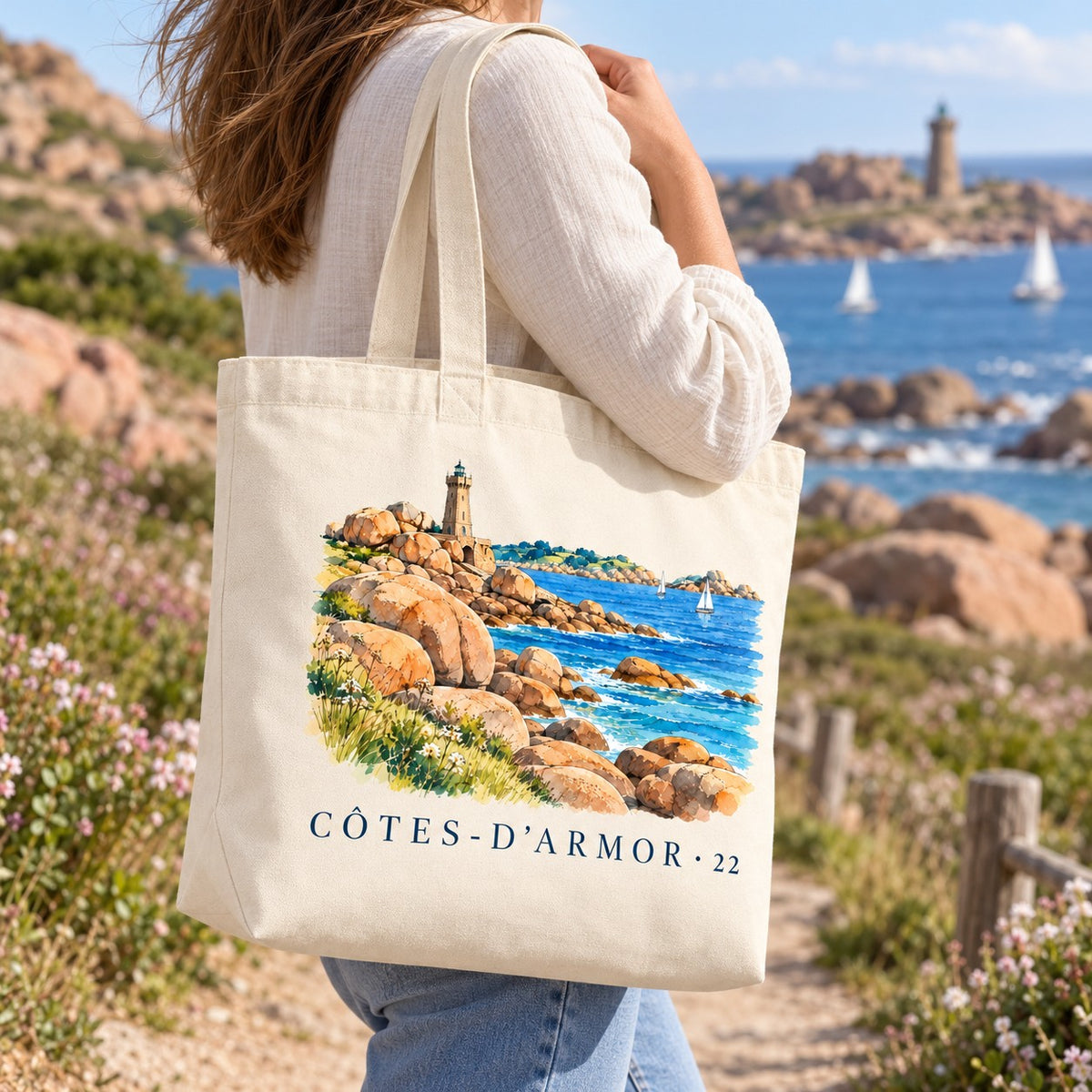 Tote bag Côtes-d'Armor (22) Premium porté à l'épaule sur un sentier côtier entre les rochers de granit rose, phare en arrière-plan
