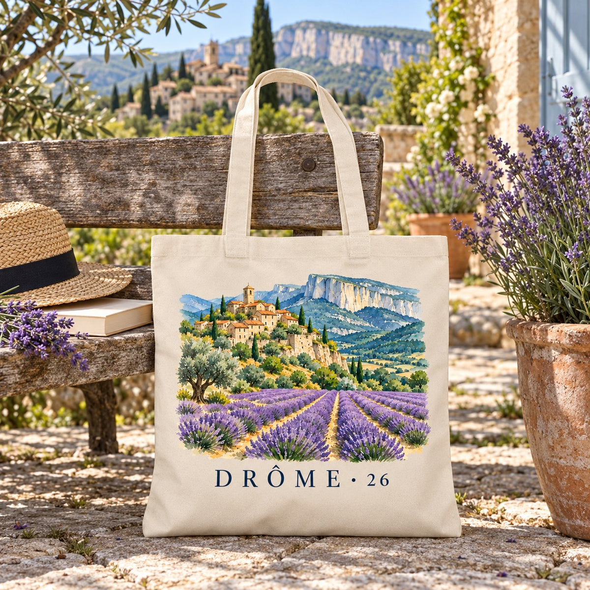 Tote bag Drôme (26) Essentiel posé sur un banc en terrasse, avec un chapeau de paille et un pot de lavande