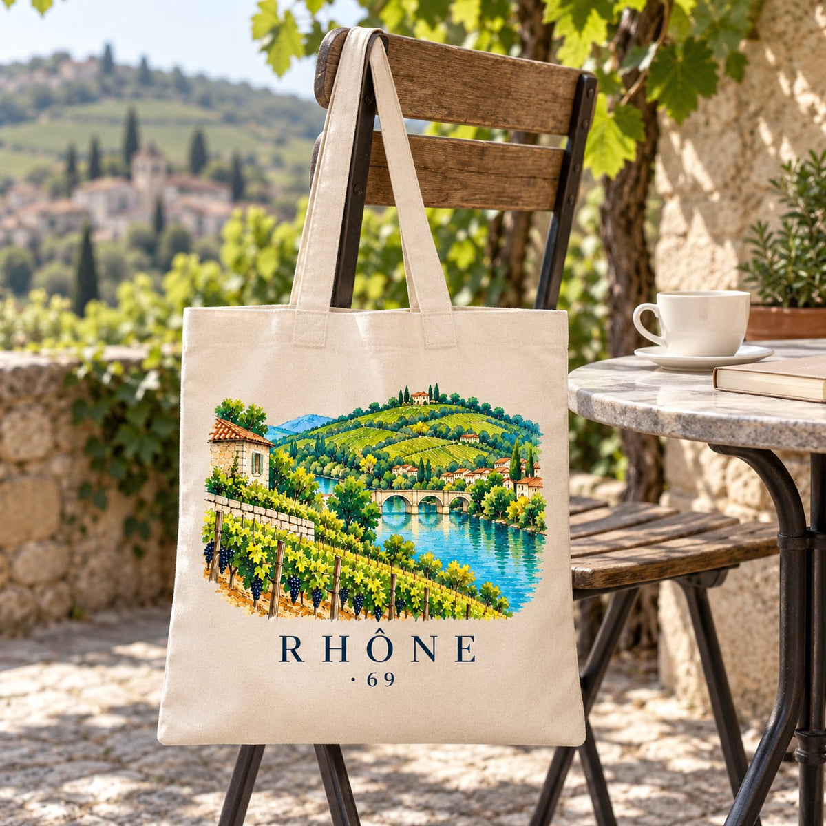 Tote bag Rhône (69) Essentiel suspendu à une chaise en terrasse face aux vignes, avec un café