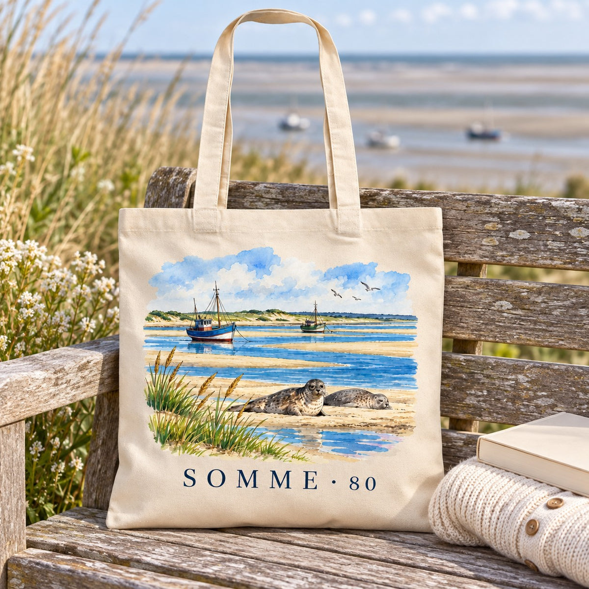 Tote bag Somme (80) Essentiel posé sur un banc face à la baie, avec un livre et un pull