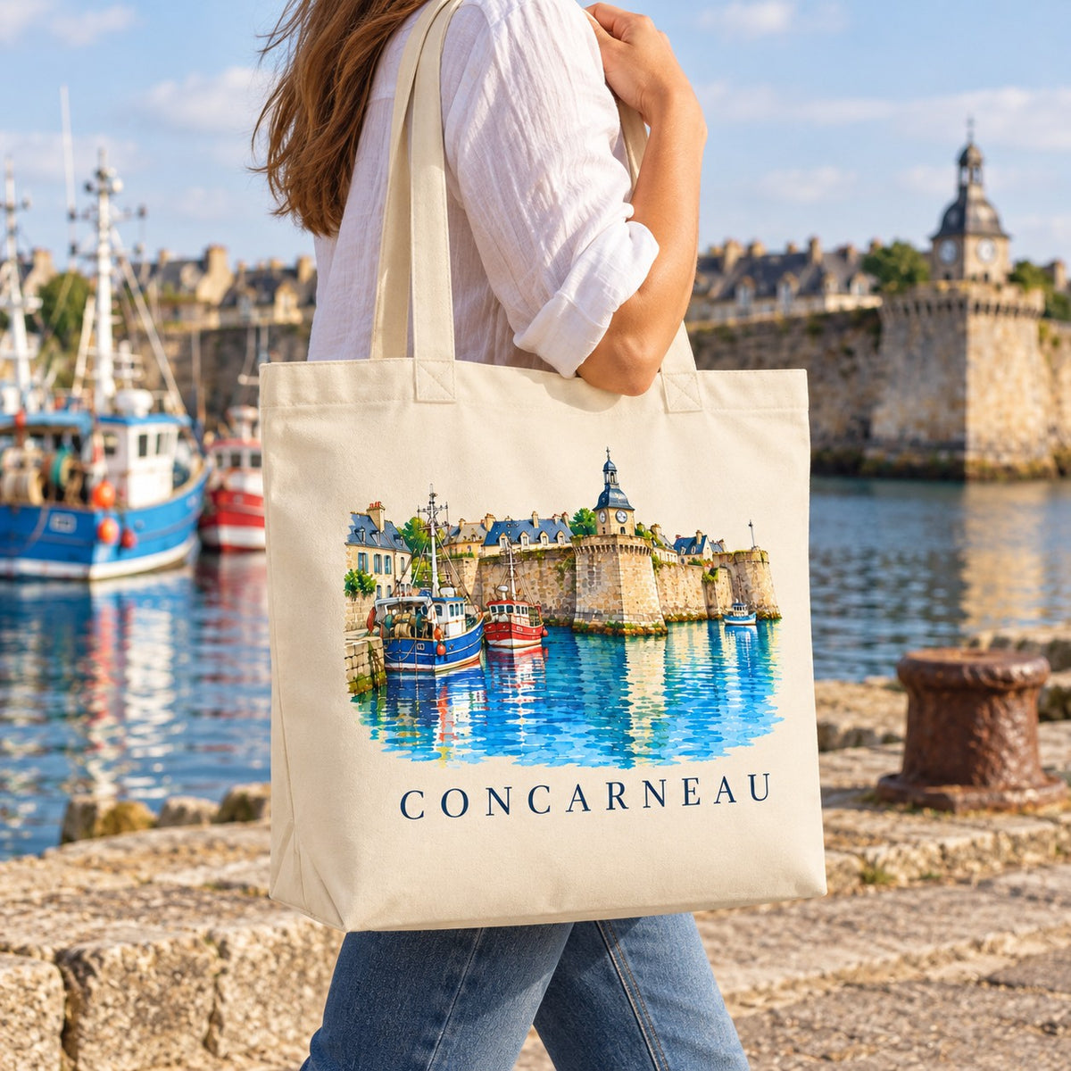 Tote bag Concarneau Premium porté à l'épaule sur un quai du port, Ville Close en arrière-plan
