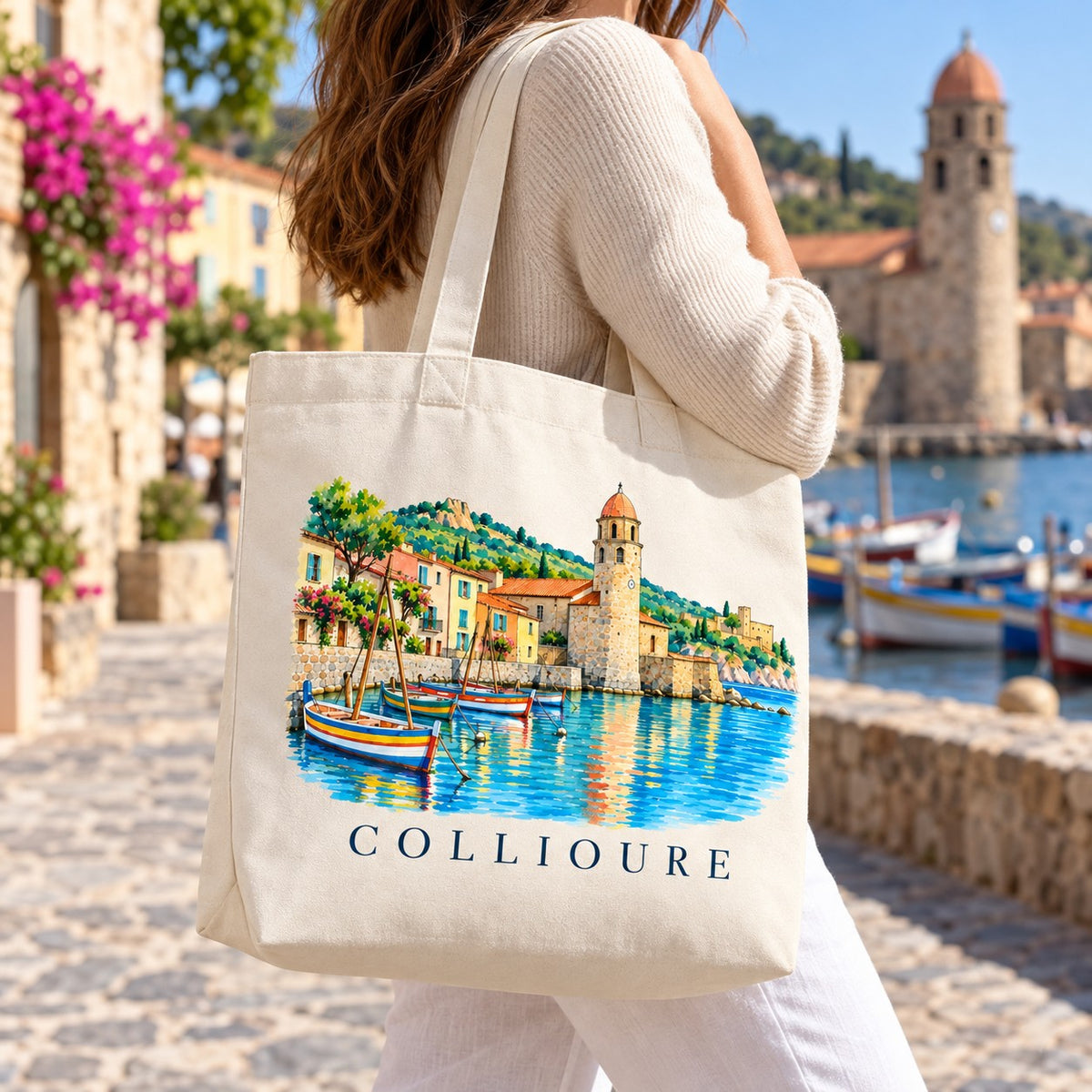 Tote bag Collioure Premium porté à l'épaule sur le quai du port, clocher en arrière-plan