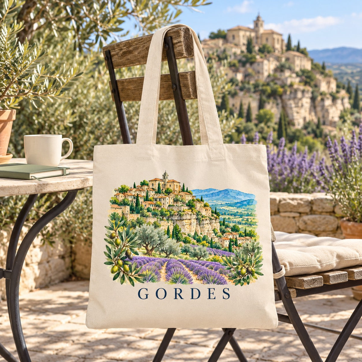 Tote bag Gordes Essentiel suspendu à une chaise de bistrot en terrasse face au village perché