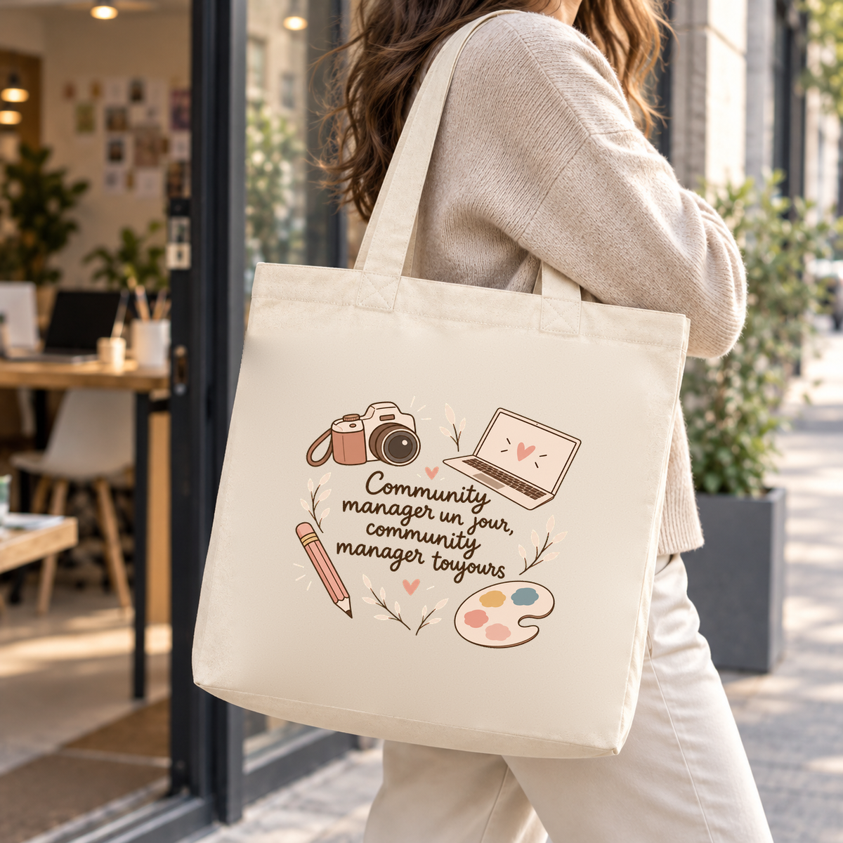 Tote bag community manager Premium porté à l'épaule dans la rue, devant un espace de coworking