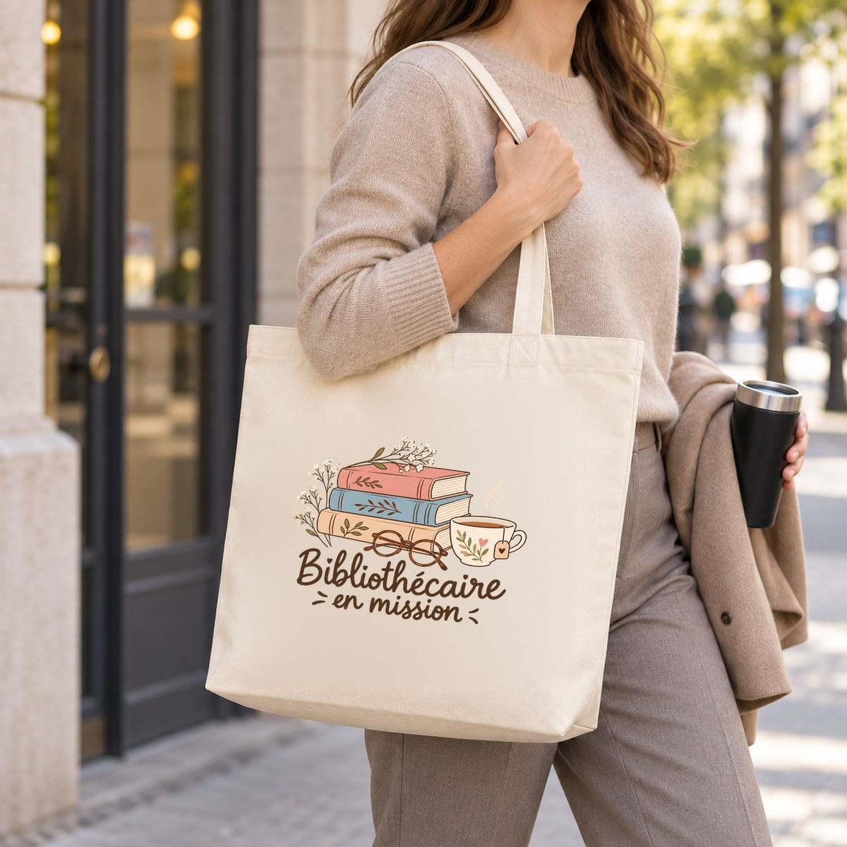Tote bag bibliothécaire « Bibliothécaire en mission » Premium porté à l'épaule devant une bibliothèque, une gourde à la main