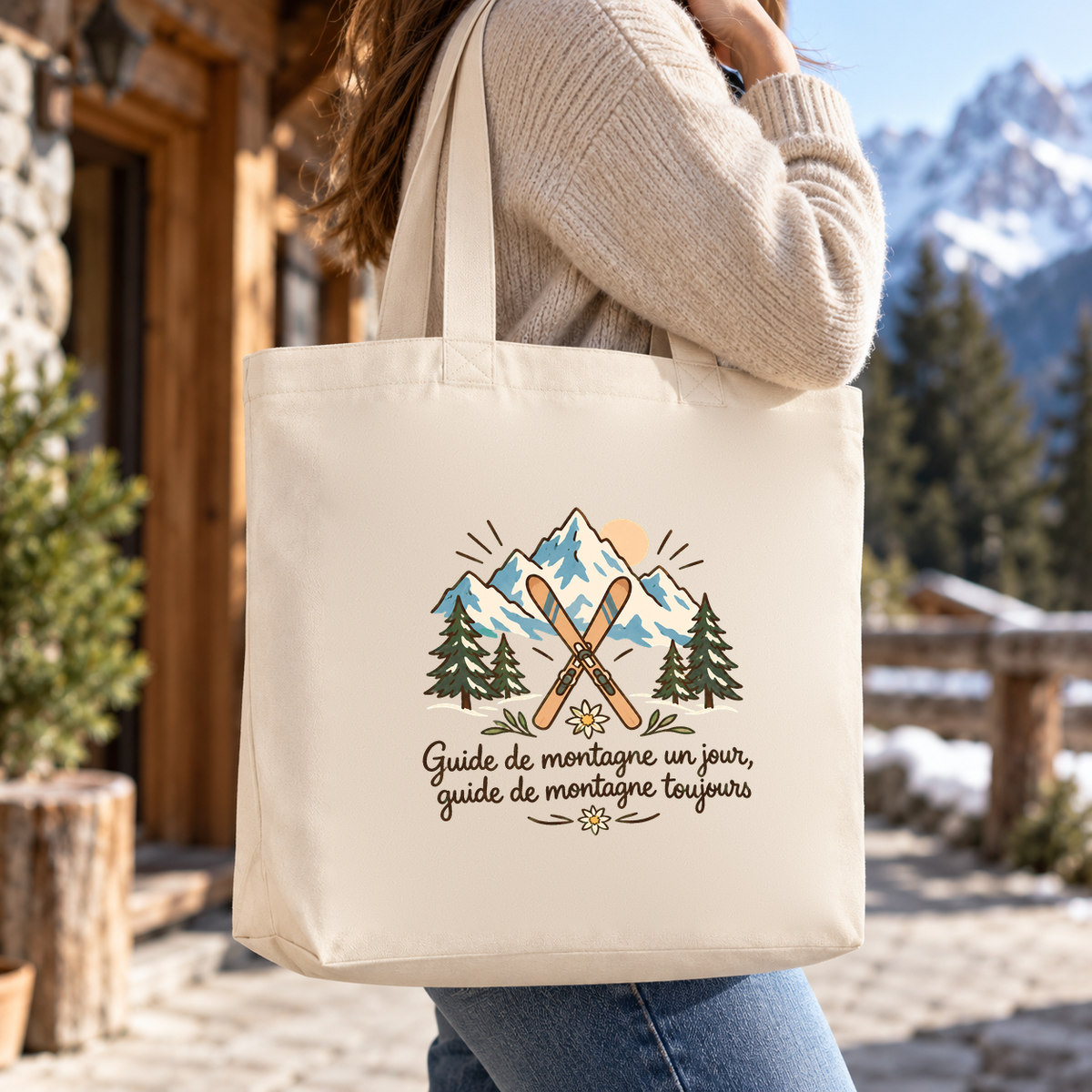 Tote bag guide de montagne Premium porté à l'épaule devant un chalet de montagne