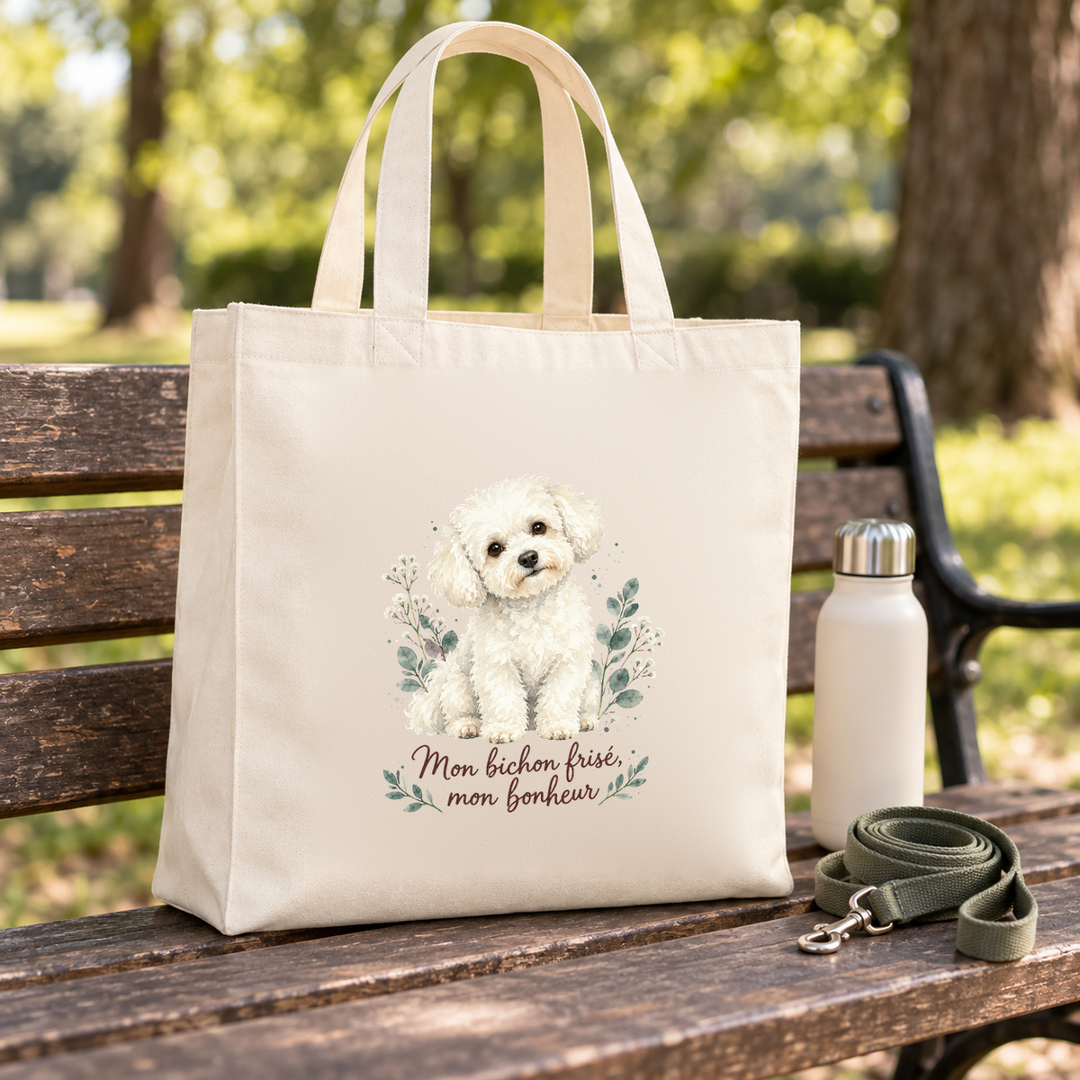 Tote bag bichon frisé « Mon bichon frisé, mon bonheur » Premium posé sur un banc de parc, à côté d'une gourde et d'une laisse