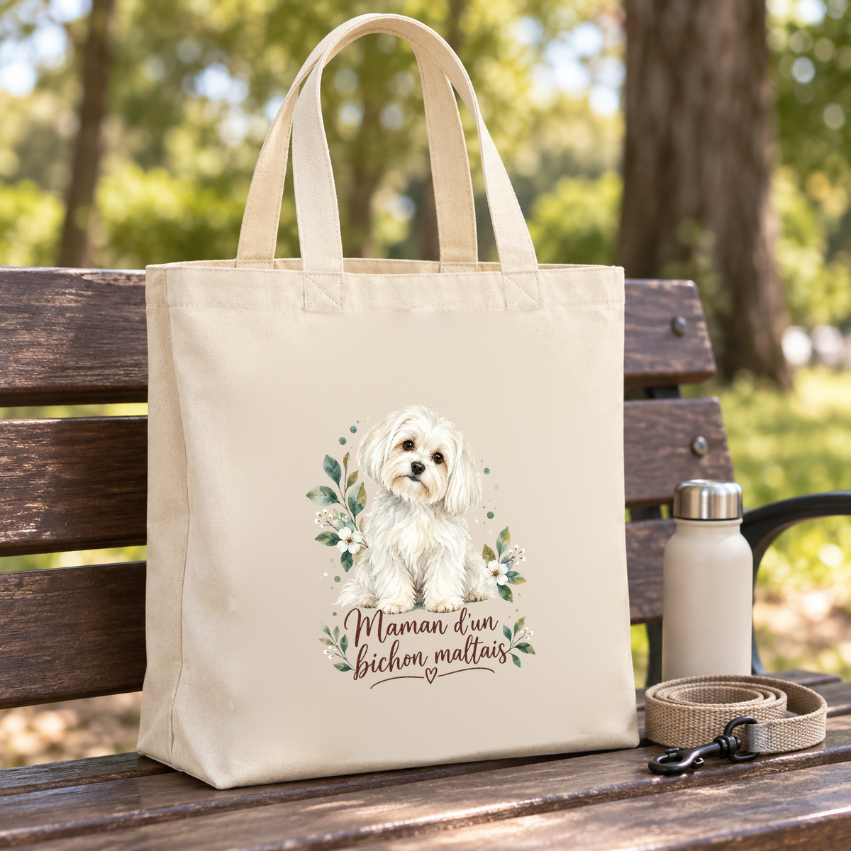 Tote bag bichon maltais « Maman d'un bichon maltais » Premium posé sur un banc de parc, à côté d'une gourde et d'une laisse