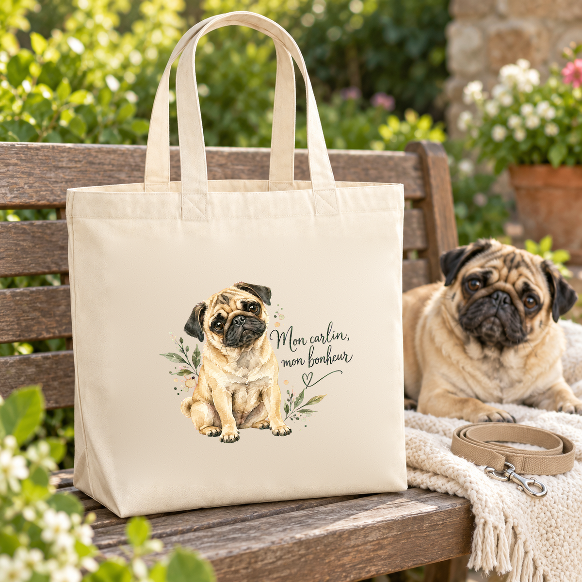 Tote bag carlin « Mon carlin, mon bonheur » Premium posé sur un banc de jardin à côté d'un carlin, sur un plaid