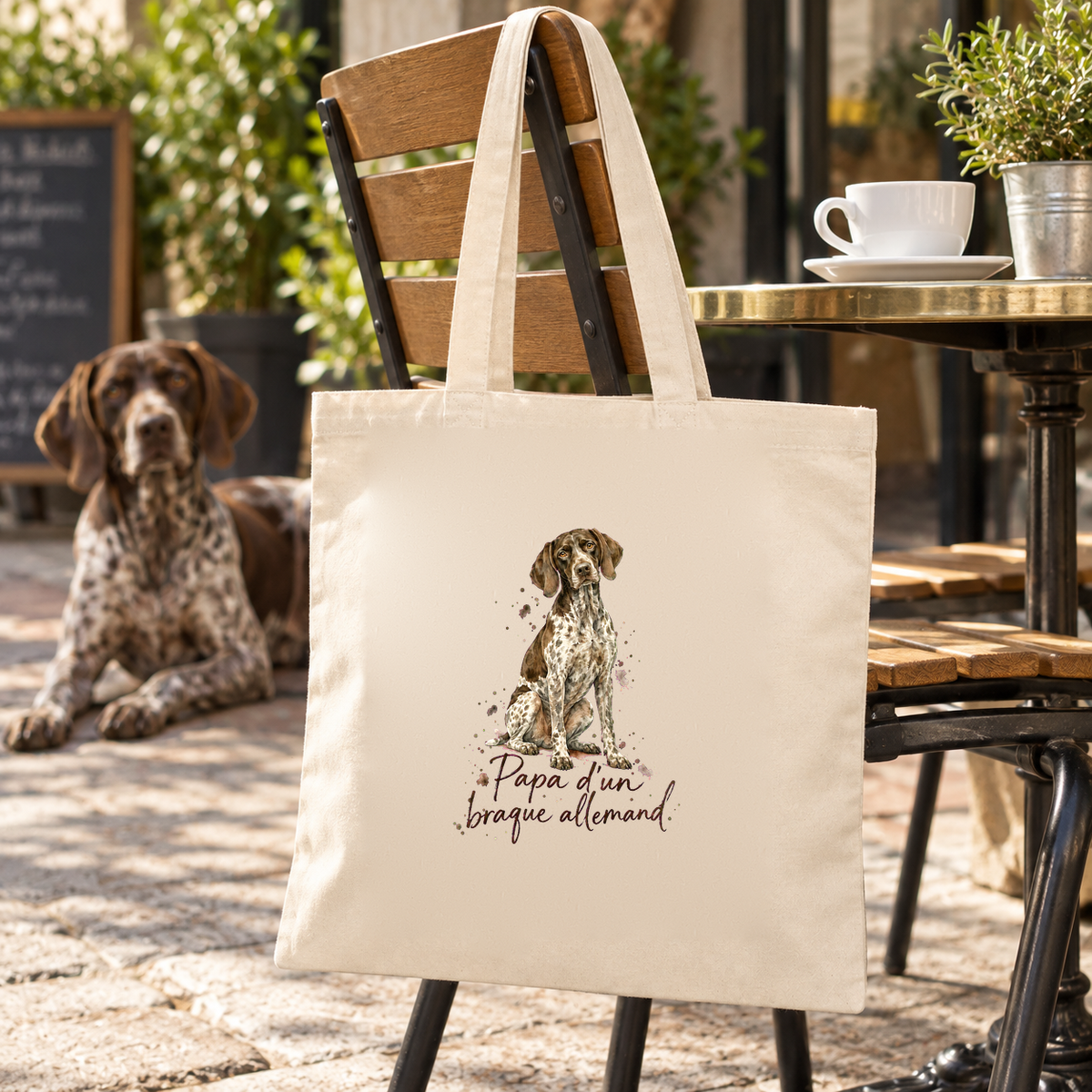Tote bag braque allemand « Papa d'un braque allemand » Essentiel suspendu à une chaise de terrasse de café, à côté d'une tasse et d'un braque allemand