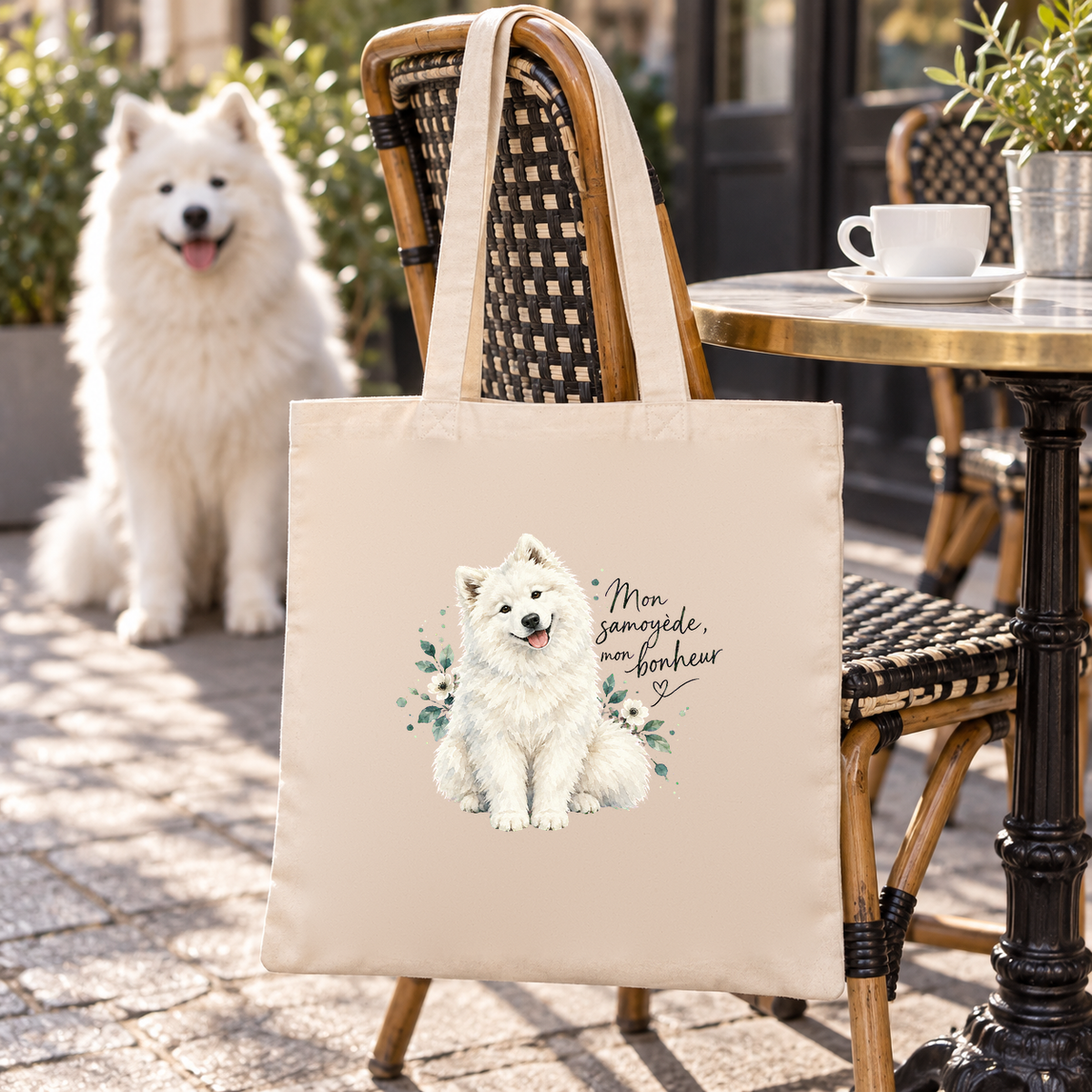 Tote bag samoyède « Mon samoyède, mon bonheur » Essentiel suspendu à une chaise de terrasse de café, à côté d'une tasse et d'un samoyède