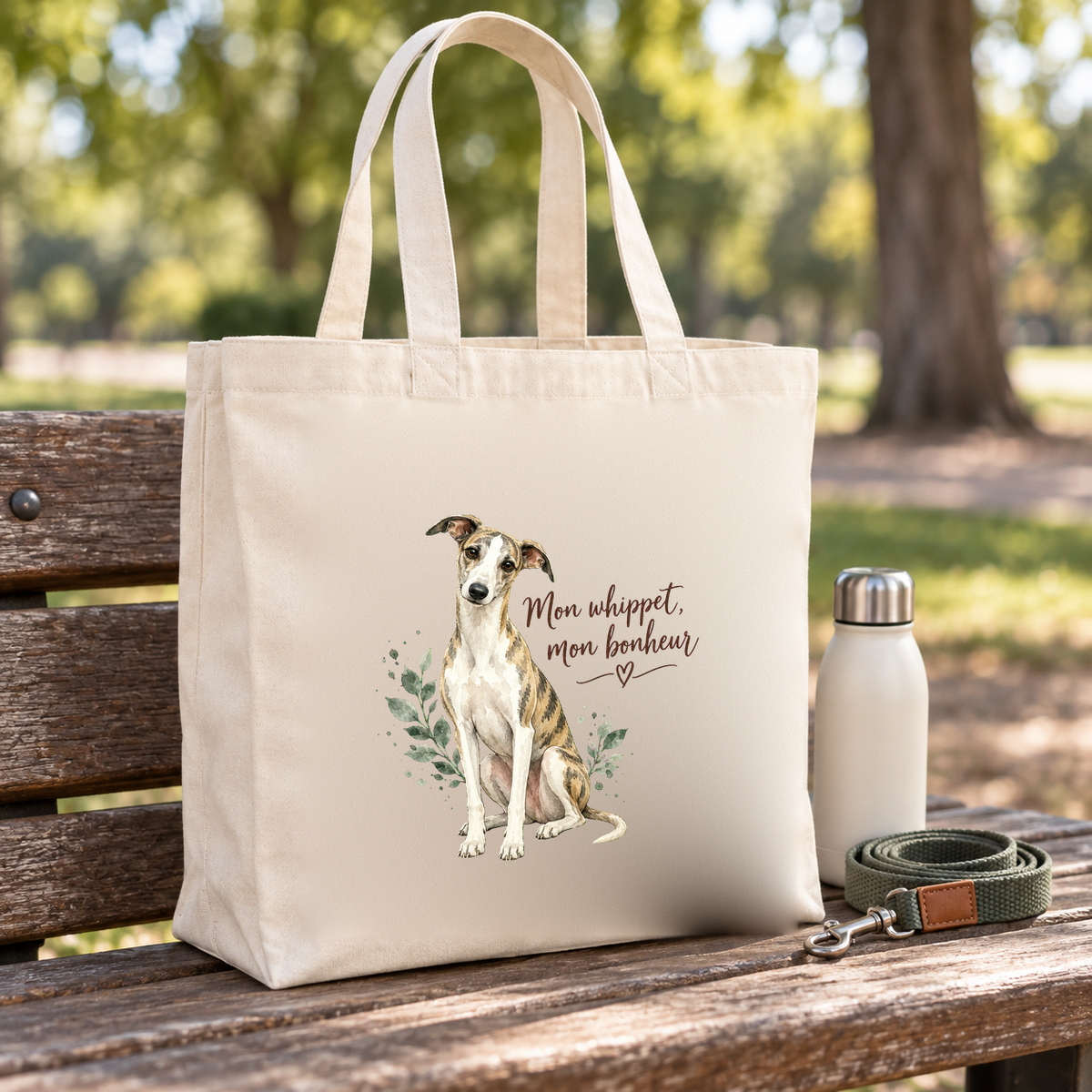 Tote bag whippet « Mon whippet, mon bonheur » Premium posé sur un banc de parc, à côté d'une gourde et d'une laisse