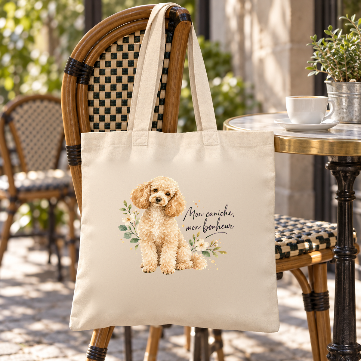 Tote bag caniche « Mon caniche, mon bonheur » Essentiel suspendu à une chaise de terrasse de café, à côté d'une tasse