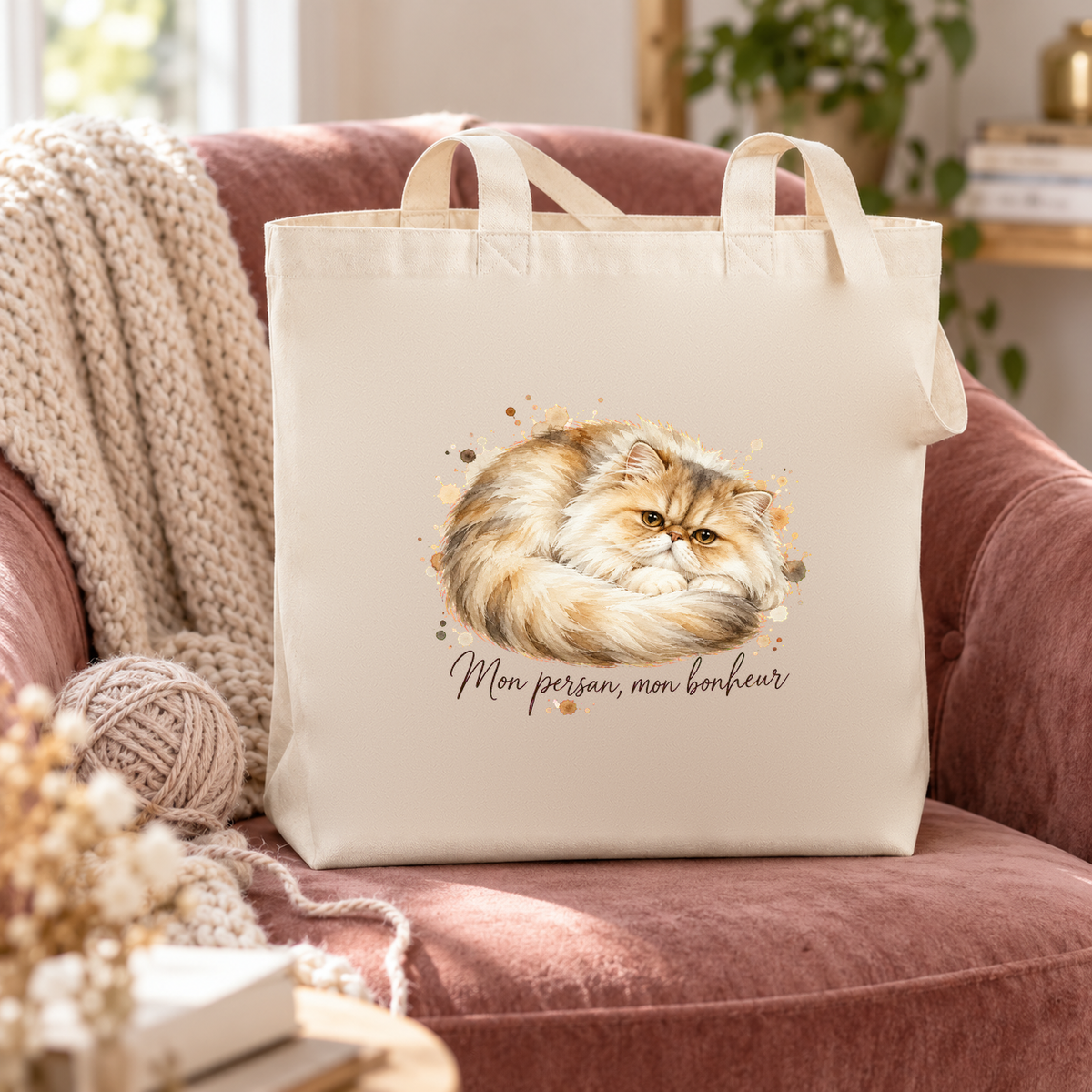 Tote bag persan « Mon persan, mon bonheur » Premium posé sur un fauteuil en velours rose, à côté d'un plaid et d'une pelote de laine