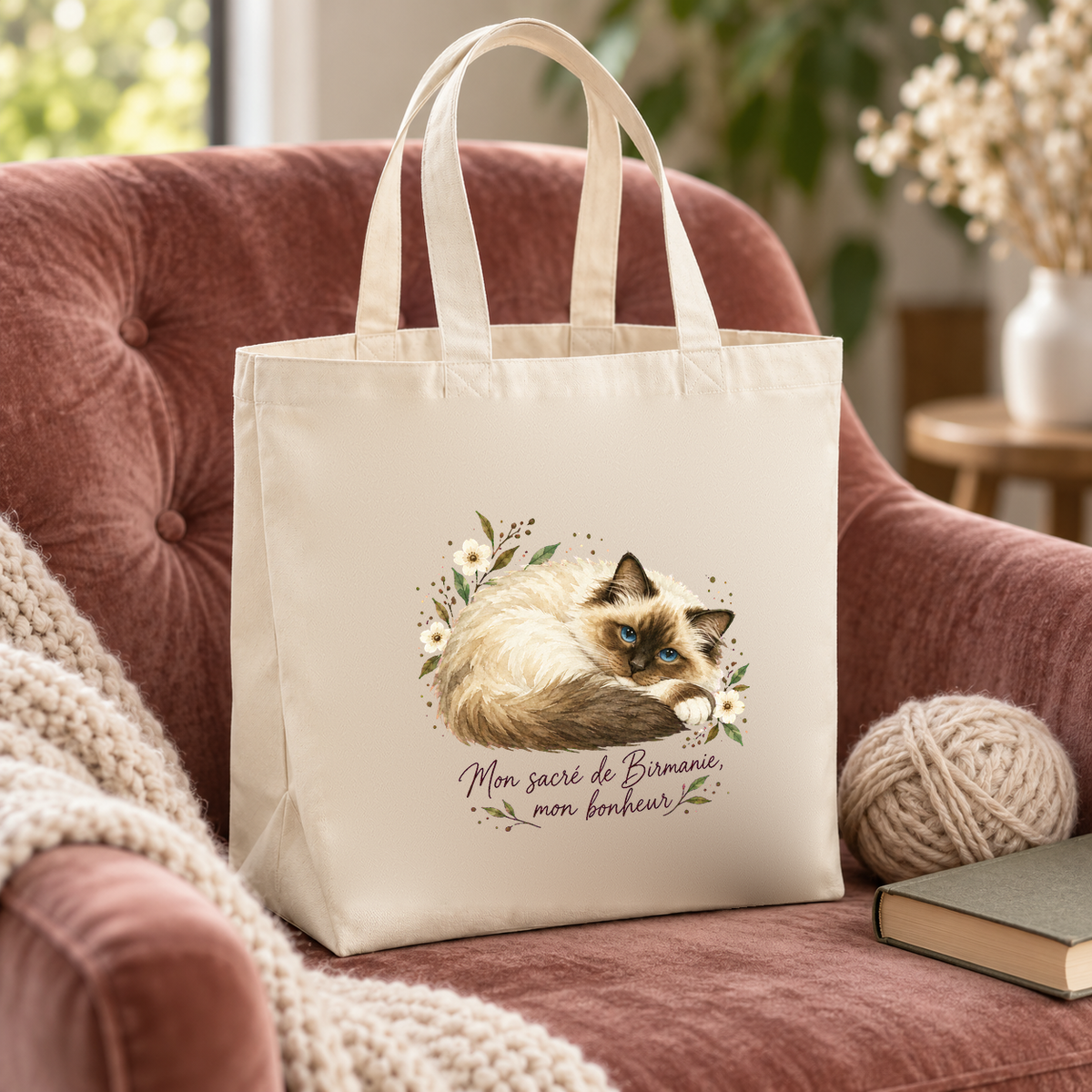 Tote bag sacré de Birmanie « Mon sacré de Birmanie, mon bonheur » Premium posé sur un fauteuil en velours vieux rose, à côté d'une pelote de laine et d'un livre