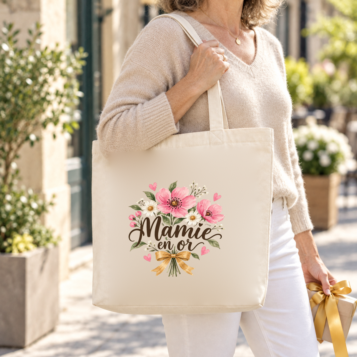 Tote bag mamie « Mamie en or » Premium porté à l'épaule dans une rue fleurie