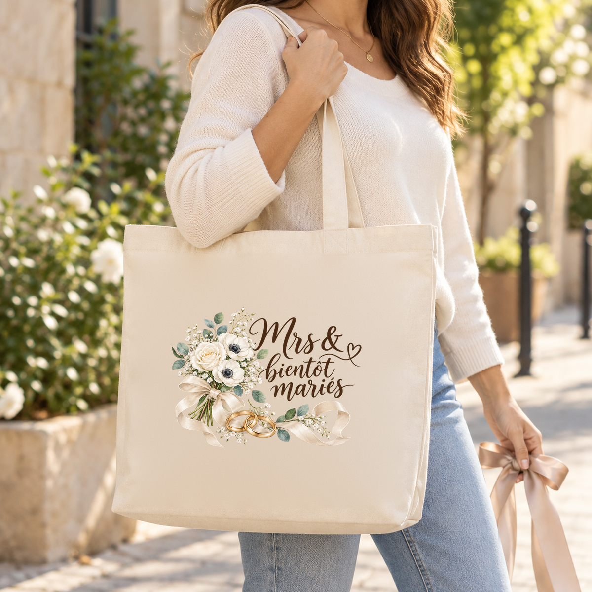 Tote bag mariage « Mrs & bientôt mariés » Premium porté à l'épaule dans une ruelle fleurie de blanc