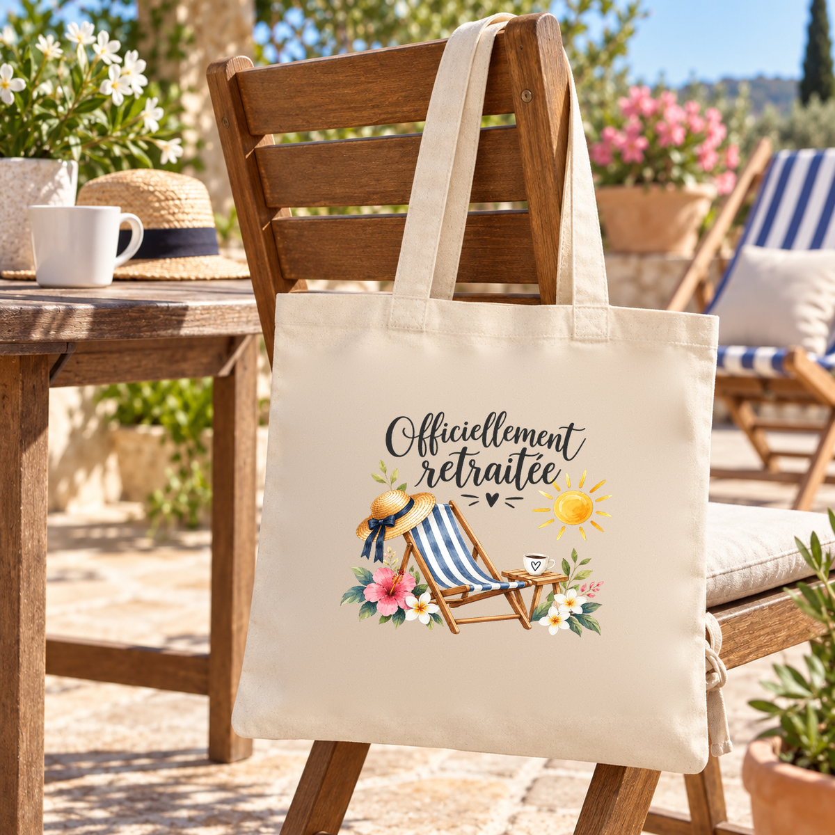 Tote bag retraite « Officiellement retraitée » Essentiel suspendu à une chaise de terrasse en bois, à côté d'une tasse de café