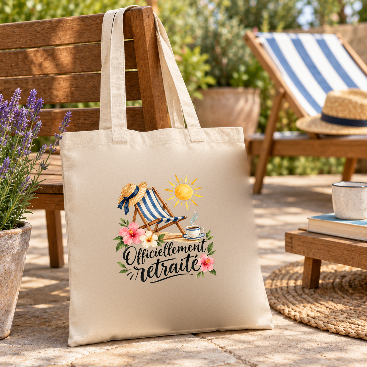 Tote bag retraite « Officiellement retraité » Essentiel suspendu à une chaise de jardin en bois, devant un transat rayé