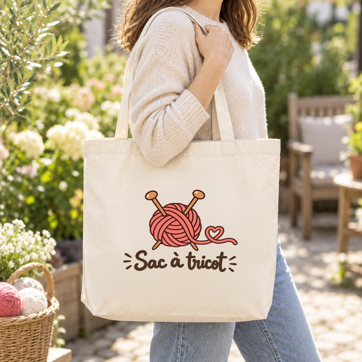 Tote bag « Sac à tricot » Premium porté à l'épaule dans un jardin, à côté d'un panier de pelotes