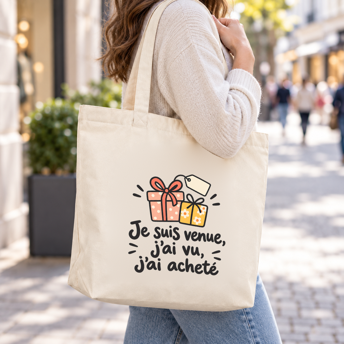 Tote bag « Je suis venue, j'ai vu, j'ai acheté » Premium porté à l'épaule dans une rue commerçante