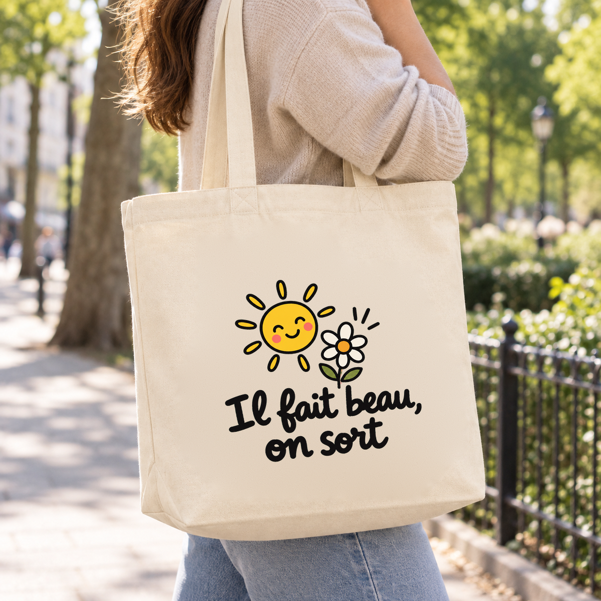 Tote bag « Il fait beau, on sort » Premium porté à l'épaule lors d'une promenade dans un parc