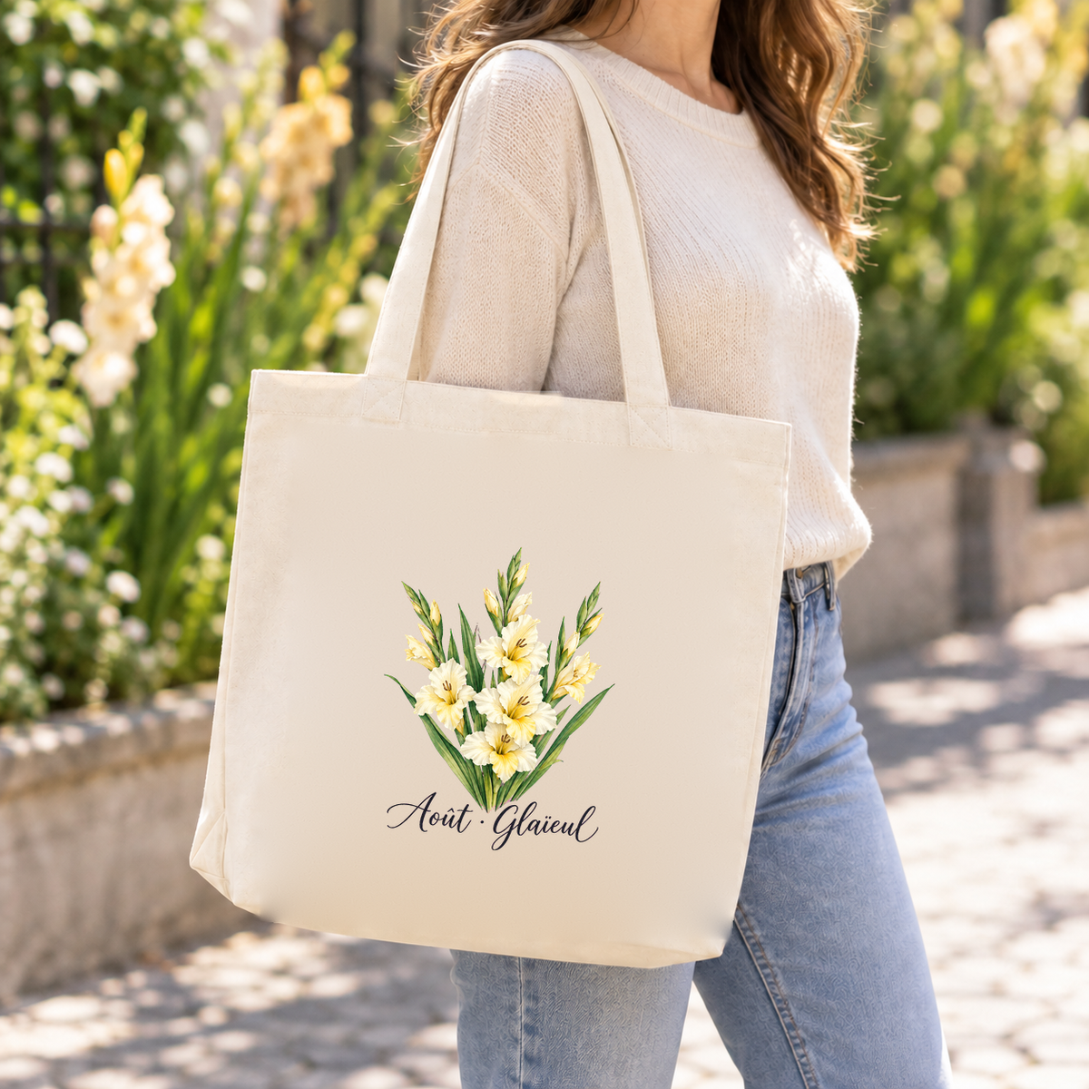 Tote bag fleur de naissance « Août · Glaïeul » Premium porté à l'épaule dans un jardin ensoleillé bordé de glaïeuls