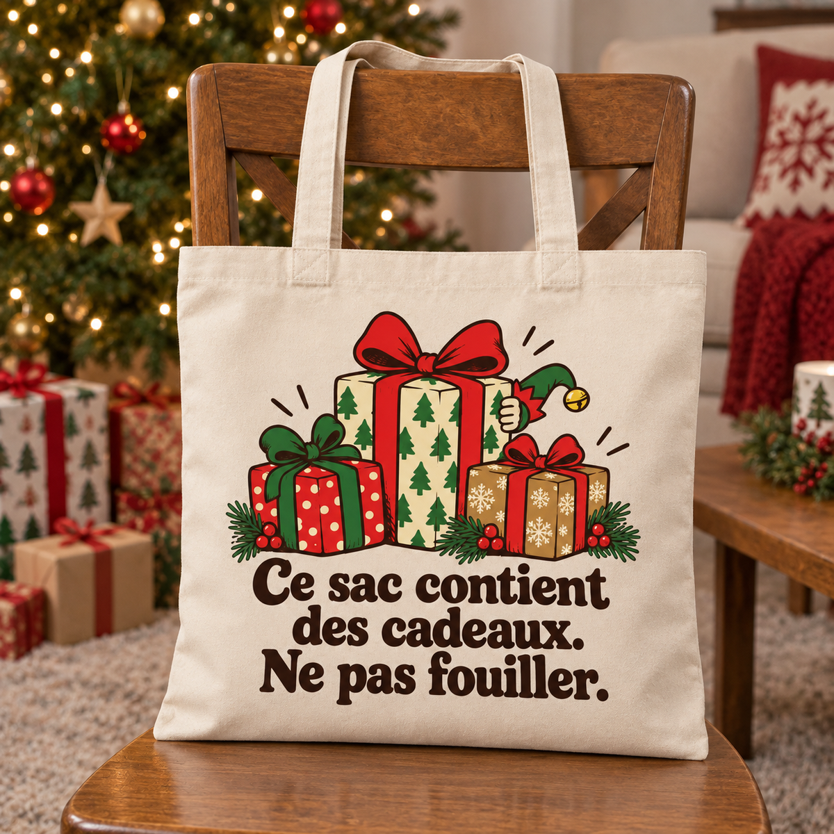 Tote bag Noël « Ce sac contient des cadeaux. Ne pas fouiller. » Essentiel posé contre le dossier d'une chaise, décor de Noël en arrière-plan