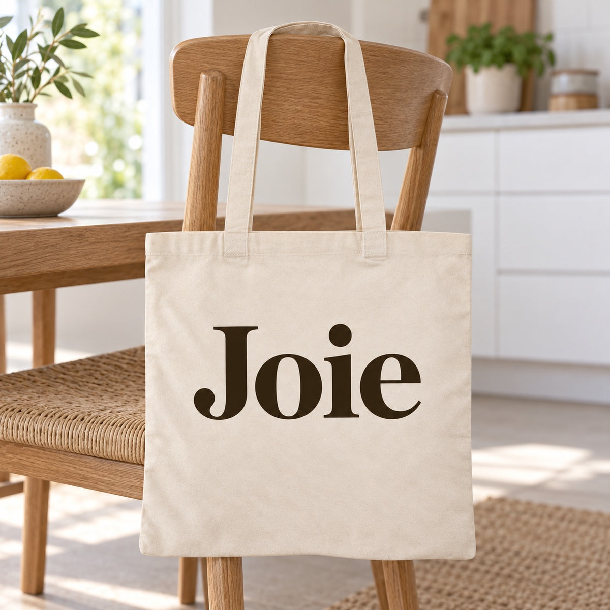 Tote bag « Joie » Essentiel posé contre une chaise dans un intérieur clair