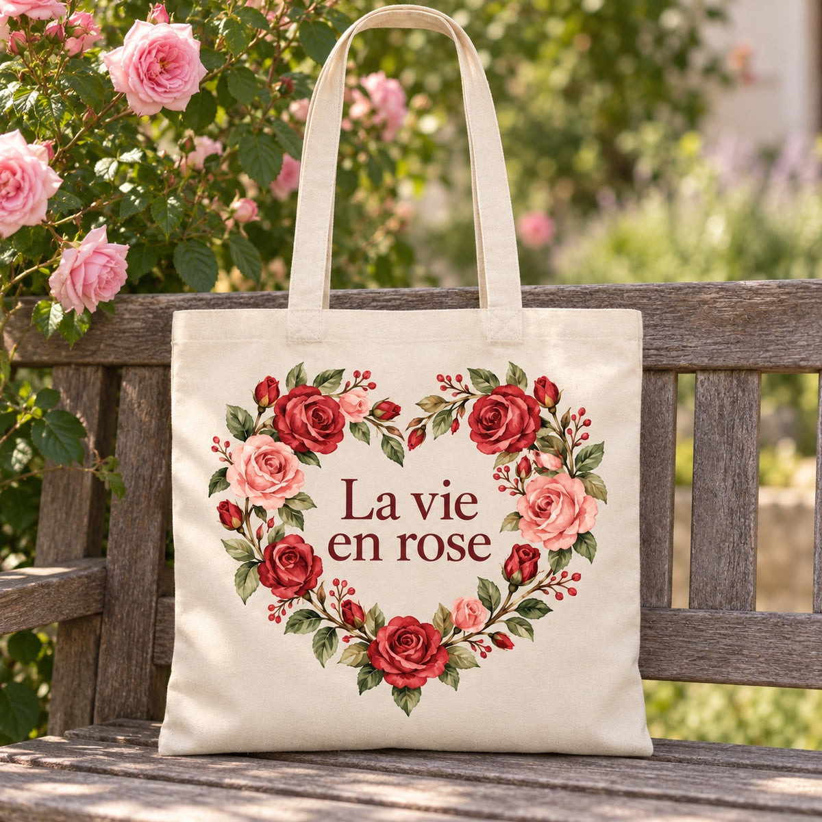 Tote bag « La vie en rose » Essentiel appuyé contre un banc de jardin près d'un rosier