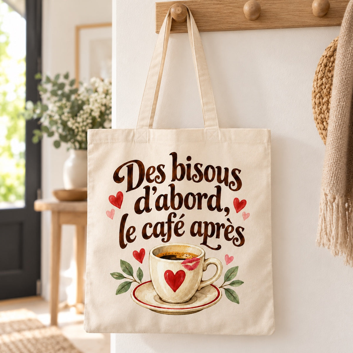 Tote bag « Des bisous d’abord, le café après » Essentiel suspendu à une patère dans une entrée lumineuse