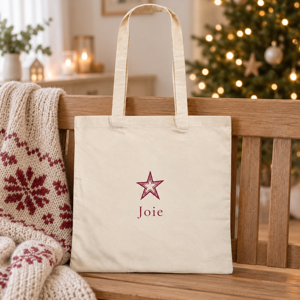 Tote bag de Noël « Joie » Essentiel appuyé contre un banc près d'un plaid de Noël