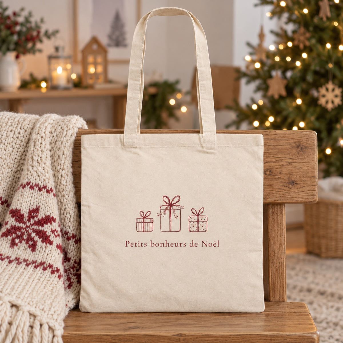 Tote bag de Noël « Petits bonheurs de Noël » Essentiel appuyé contre un banc près d'un plaid de Noël