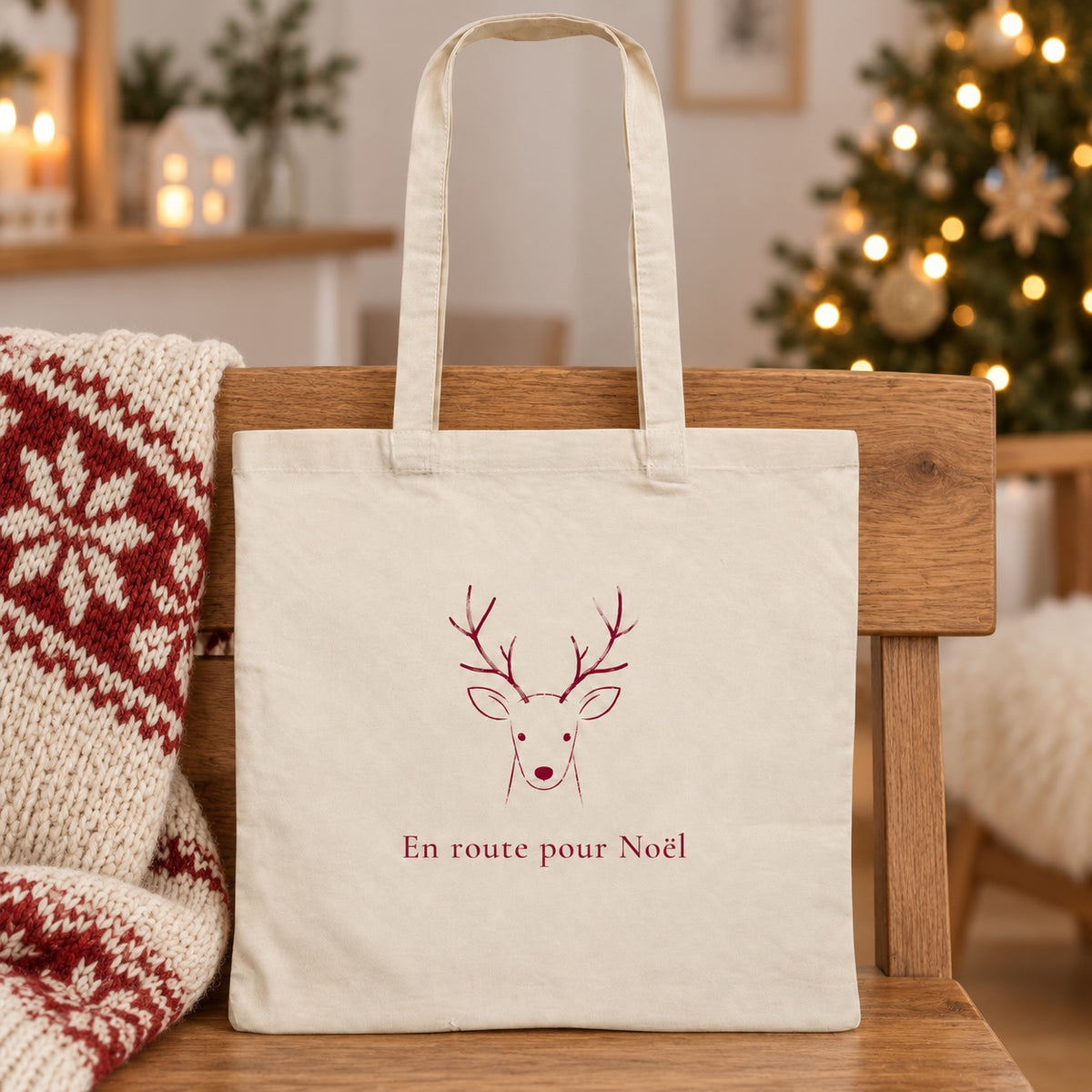 Tote bag de Noël « En route pour Noël » Essentiel appuyé contre un banc près d'un plaid de Noël