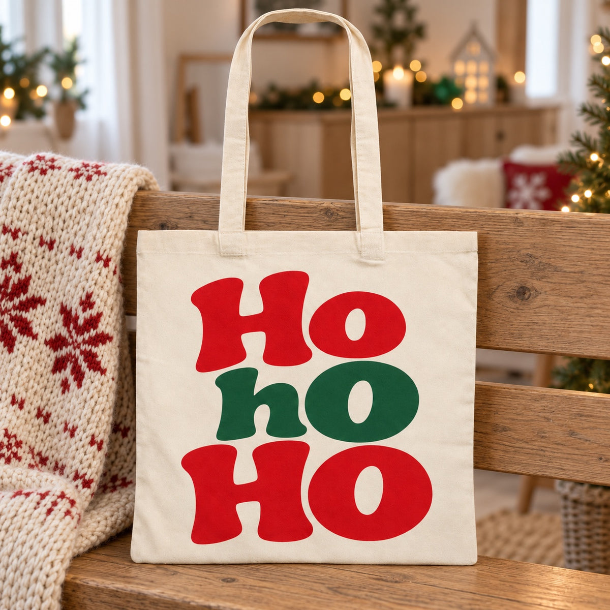 Tote bag de Noël « Ho ho ho » Essentiel appuyé contre un banc près d'un plaid de Noël