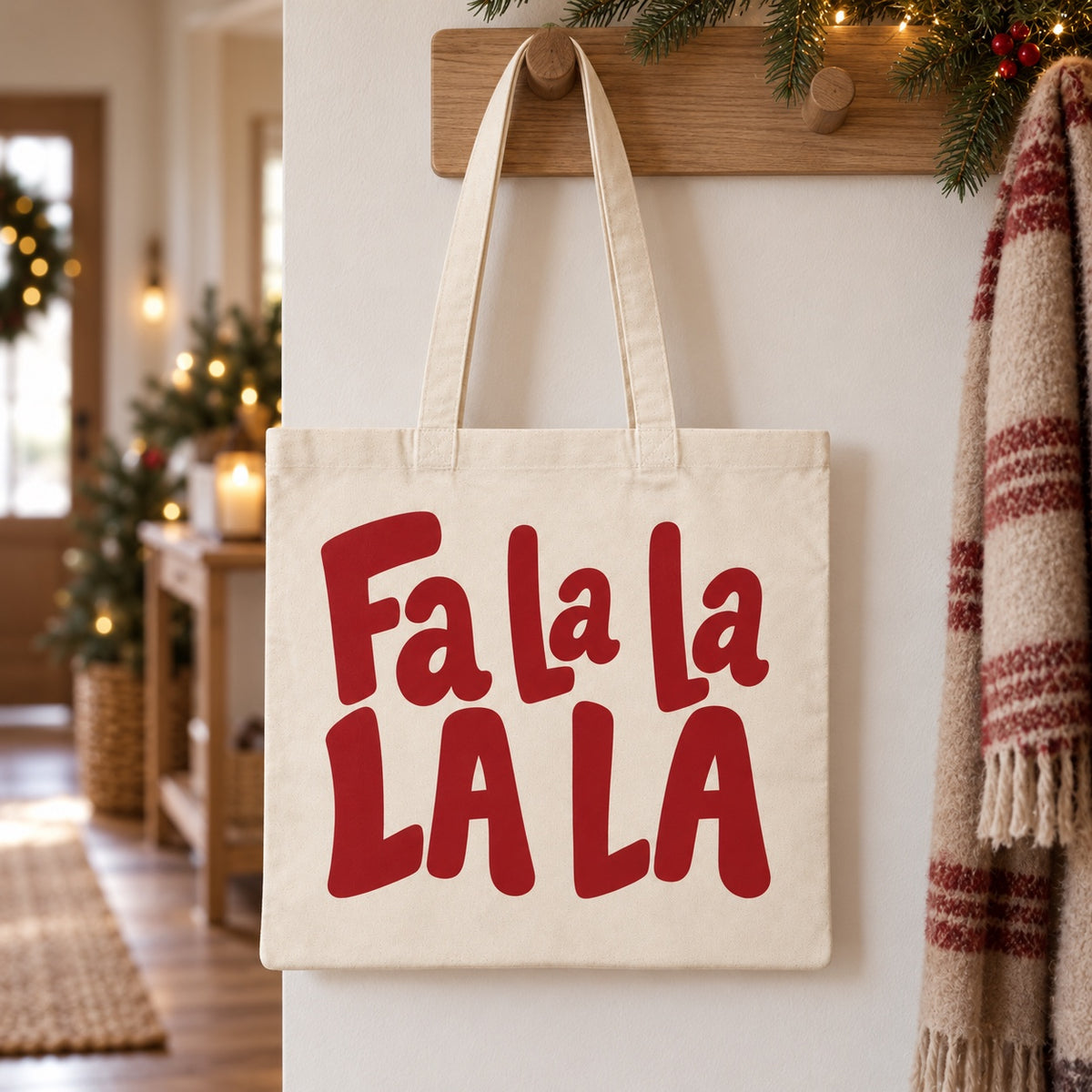 Tote bag de Noël « Fa la la la la » Essentiel suspendu à une patère dans une entrée décorée pour Noël