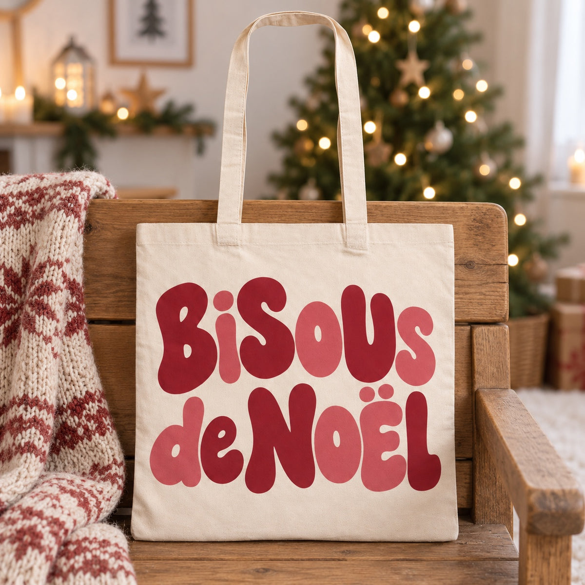 Tote bag de Noël « Bisous de Noël » Essentiel appuyé contre un banc près d'un plaid de Noël