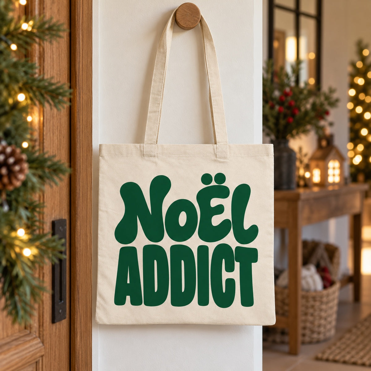 Tote bag de Noël « Noël addict » Essentiel suspendu à une patère dans une entrée décorée pour Noël