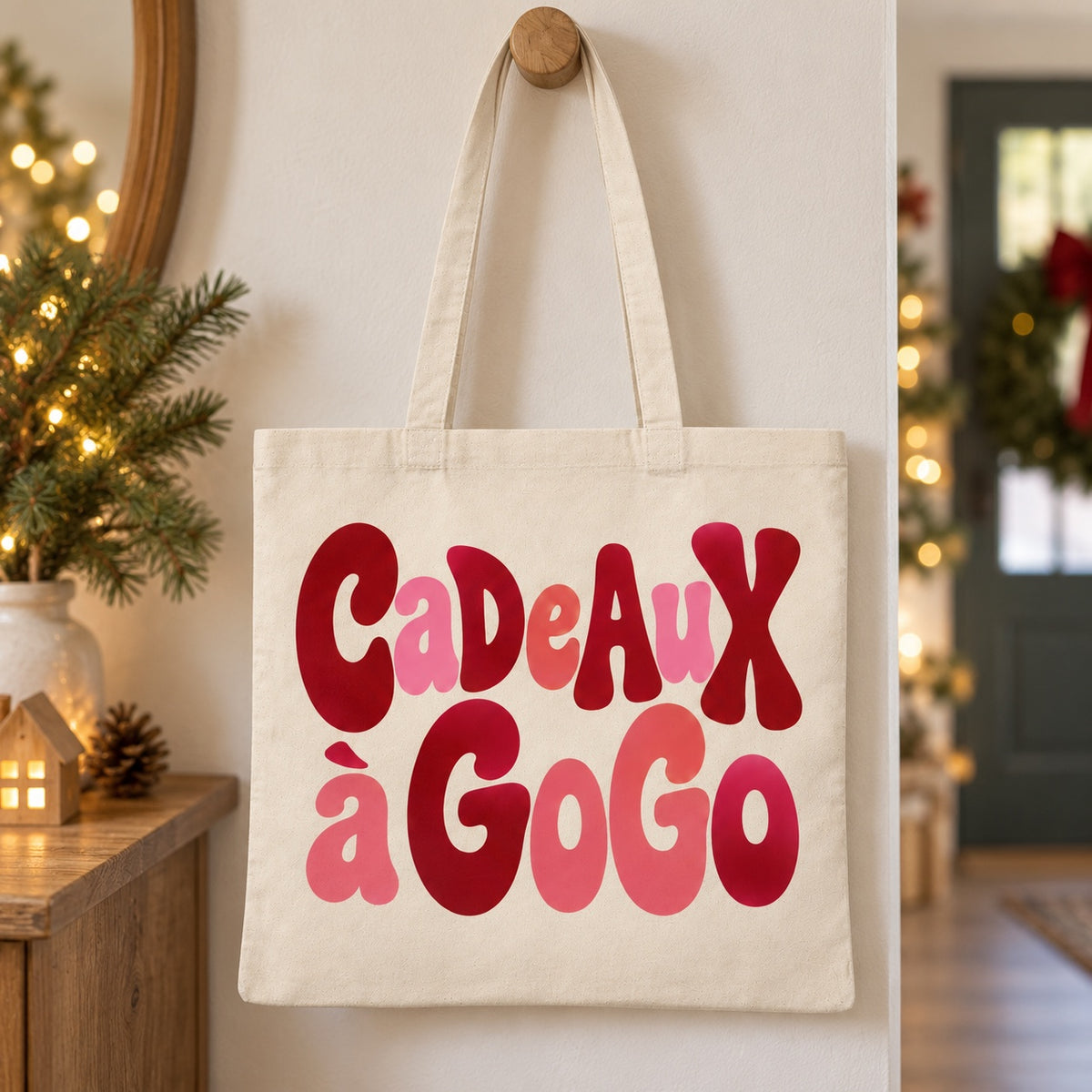 Tote bag de Noël « Cadeaux à gogo » Essentiel suspendu à une patère dans une entrée décorée pour Noël